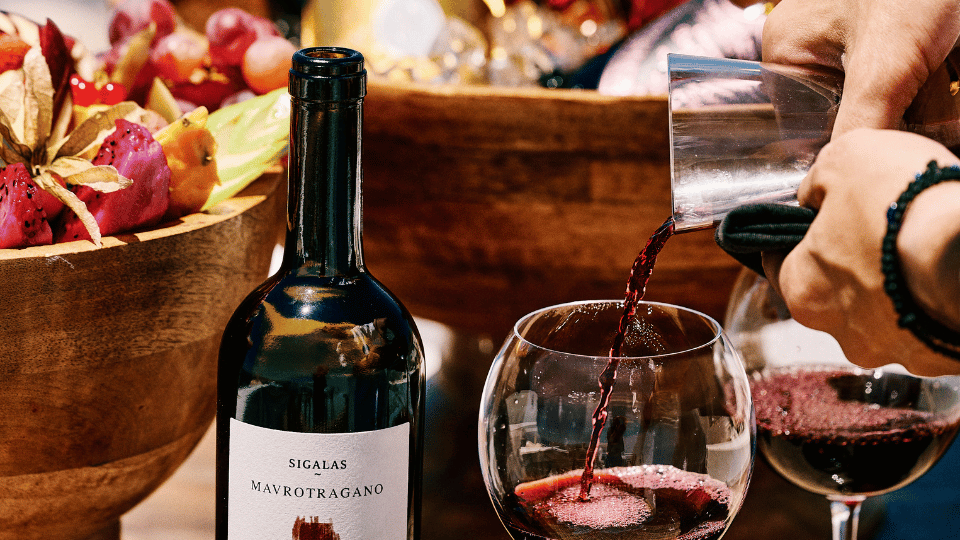 Elegant sunset wine tasting setup on a cliffside terrace in Oia, with glasses of red wine, floral centerpieces, and panoramic views of Santorini’s caldera