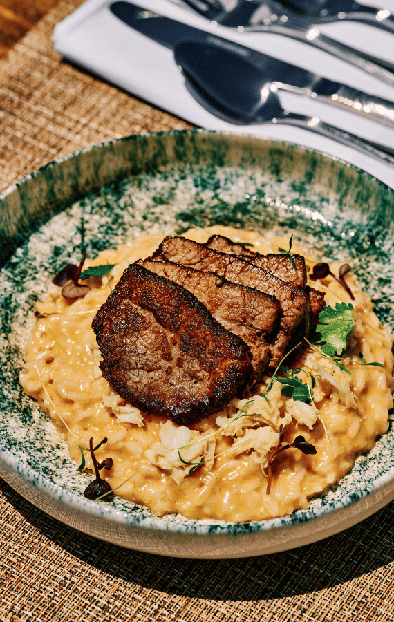 Gourmet slow-cooked beef served over creamy saffron risotto with microgreens, plated elegantly at Sunsets Terra in Santorini