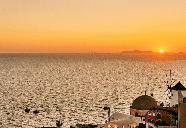 Santorini sunset over the Aegean Sea with Oia’s windmill and domed rooftops in view near Sunsets Santorini