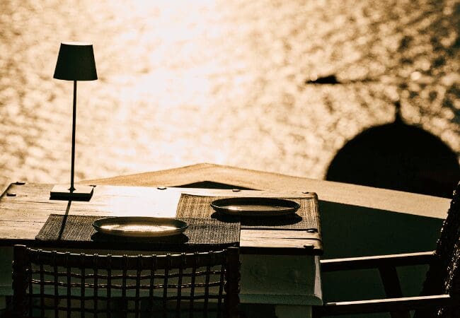 Intimate table for two at Sunsets Santorini set against golden hour reflections over the Aegean Sea and caldera dome