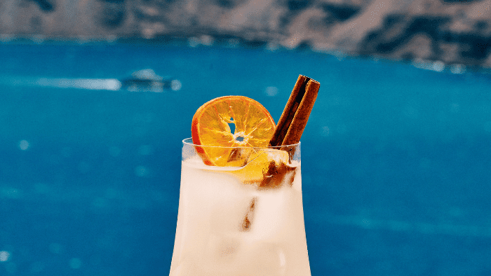 Creamy citrus cocktail with cinnamon stick garnish served with caldera views at Bites & Bubbles by Sunsets in Santorini