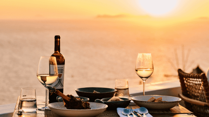 Sunset fine dining setup at Santorini Sunsets with white wine, local dishes, and panoramic Aegean Sea views