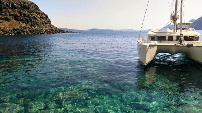 Luxury catamaran anchored in the crystal-clear waters of the Santorini caldera near volcanic cliffs.