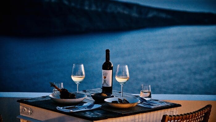Evening caldera-view dinner in Oia: wine and fine dining on a Santorini terrace under the night sky.
