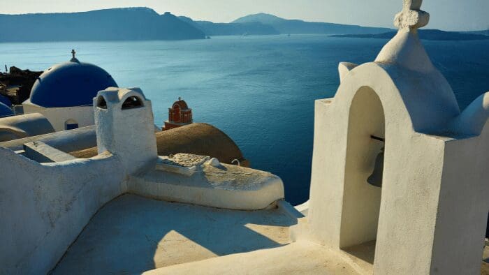 Iconic blue-domed church and white bell tower overlooking the deep blue caldera and Aegean Sea in Oia, Santorini.