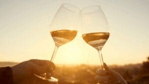Two glasses of white wine clinking at sunset, celebrating Santorini’s wine culture and romantic golden-hour views.