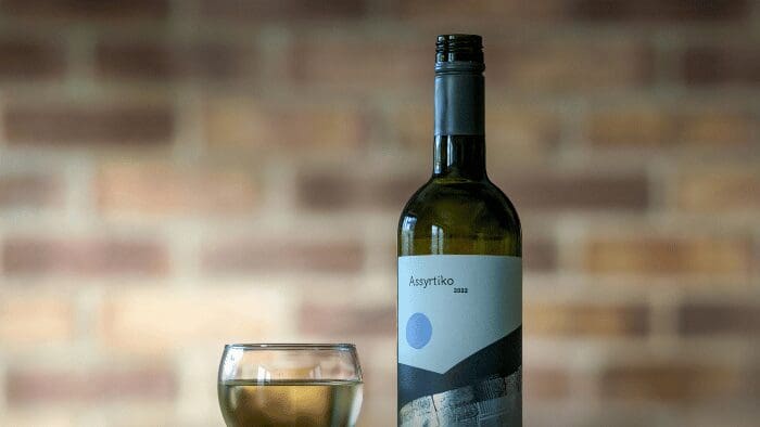 "Assyrtiko 2022 wine bottle and glass with wine, showcasing Santorini’s signature white wine made from volcanic grapes.