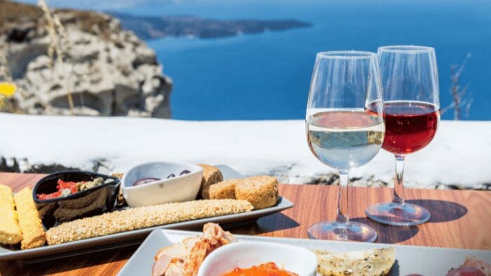 Two glasses of Santorini wine — one white and one red — paired with a Mediterranean platter featuring olives, bread, and cheese.