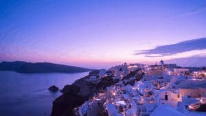 Oia windmill and glowing sunset over the Aegean Sea with illuminated white houses in Santorini.