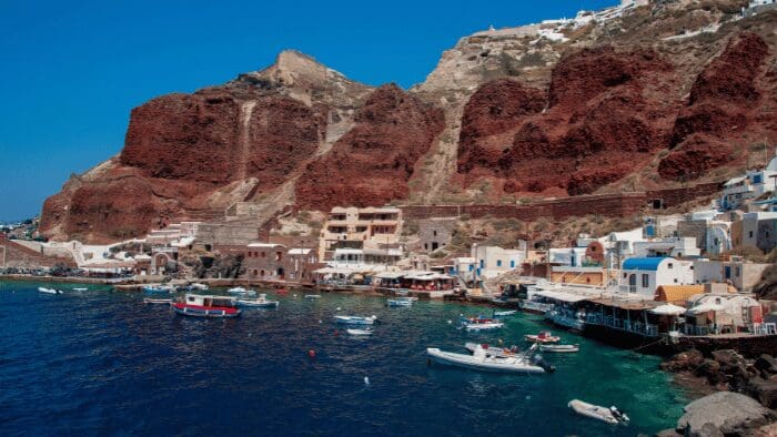 Panoramic view of Armeni Bay in Oia Santorini with volcanic cliffs, boats, and waterfront tavernas