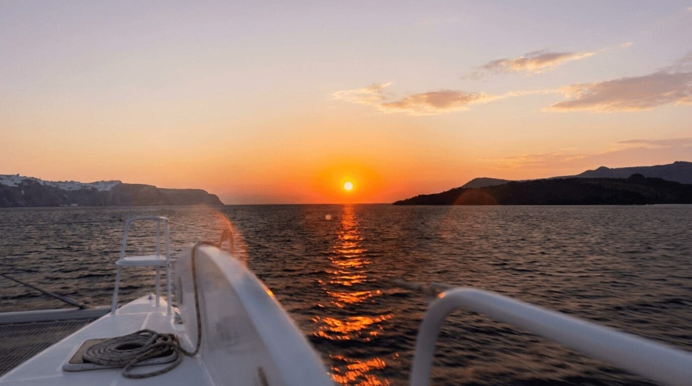 Sun setting over the Aegean Sea viewed from a catamaran deck during a Santorini sunset cruise