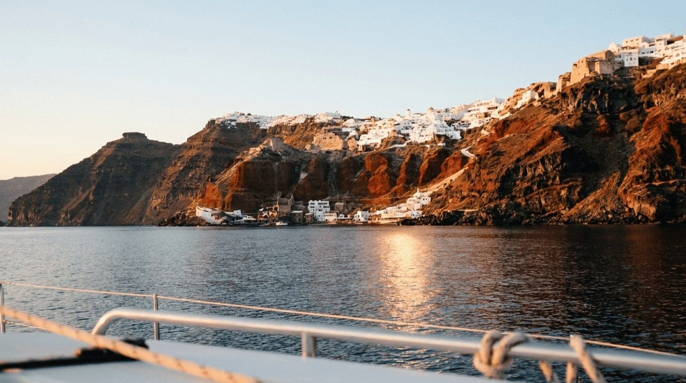 View of Oia's volcanic cliffs from a sunset cruise catamaran in the Santorini caldera at golden hour