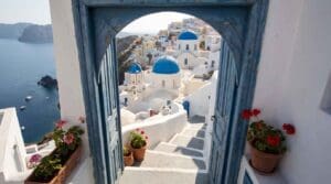 Blue-domed churches of Oia framed by a blue archway and geraniums under clear summer skies in Santorini