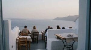 Diners at west-facing tables on a caldera-view terrace in Oia, Santorini, at sunset