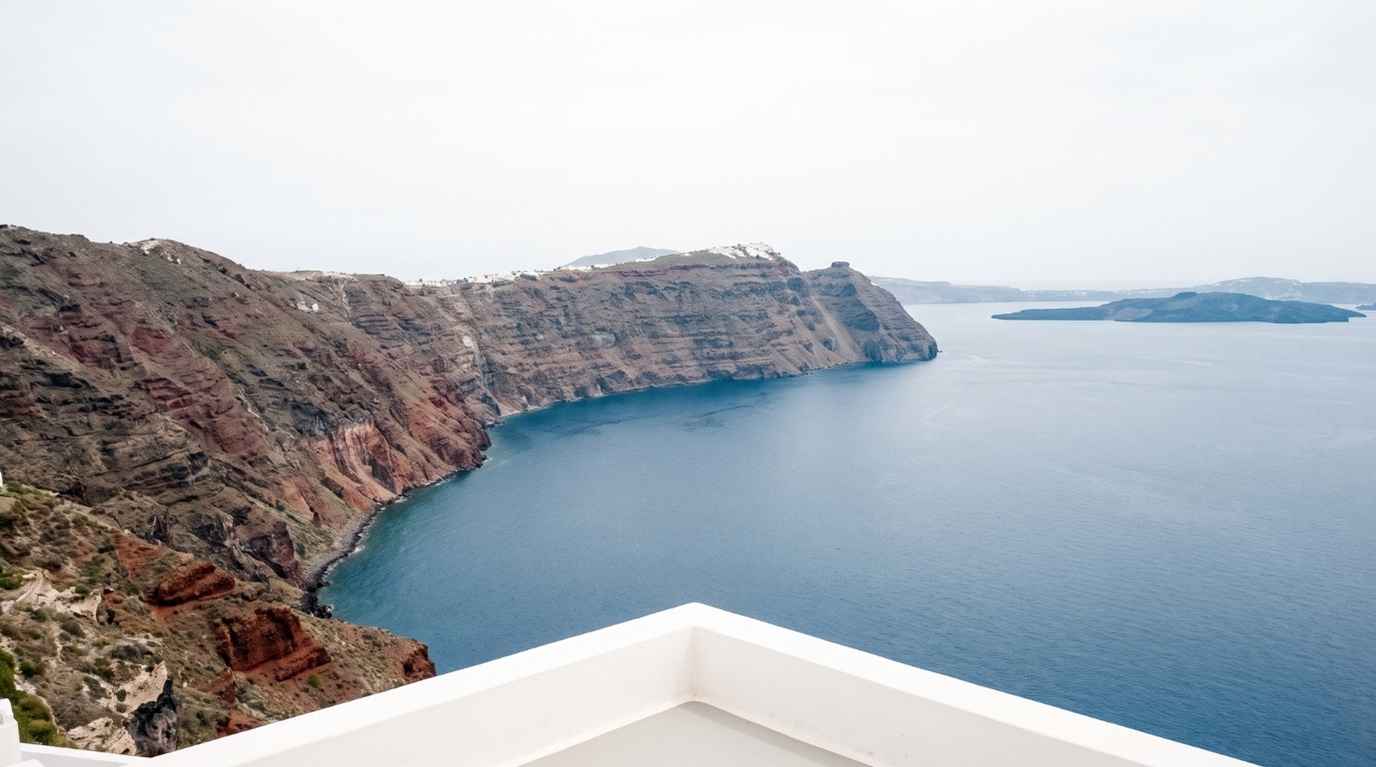 The curved volcanic cliff wall of the Santorini caldera seen from a terrace in Oia