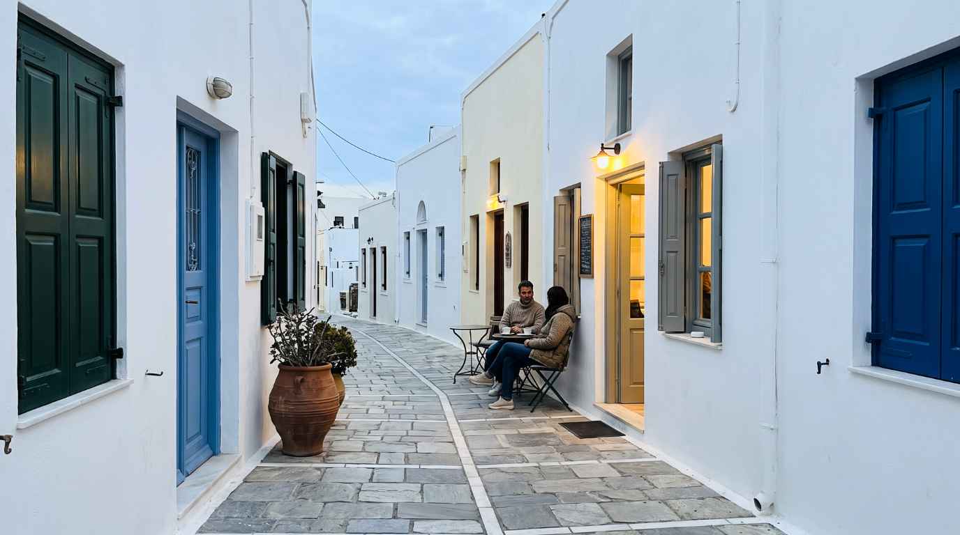 Two people having coffee outside a small café open in a quiet Santorini lane in November