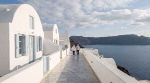 Two walkers on the quiet caldera path in Oia, Santorini, on a sunny November afternoon